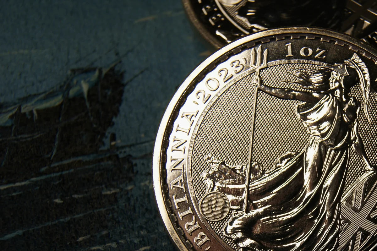 A close-up of a Royal Mint 2023 silver Britannia coin against a deep blue-green background